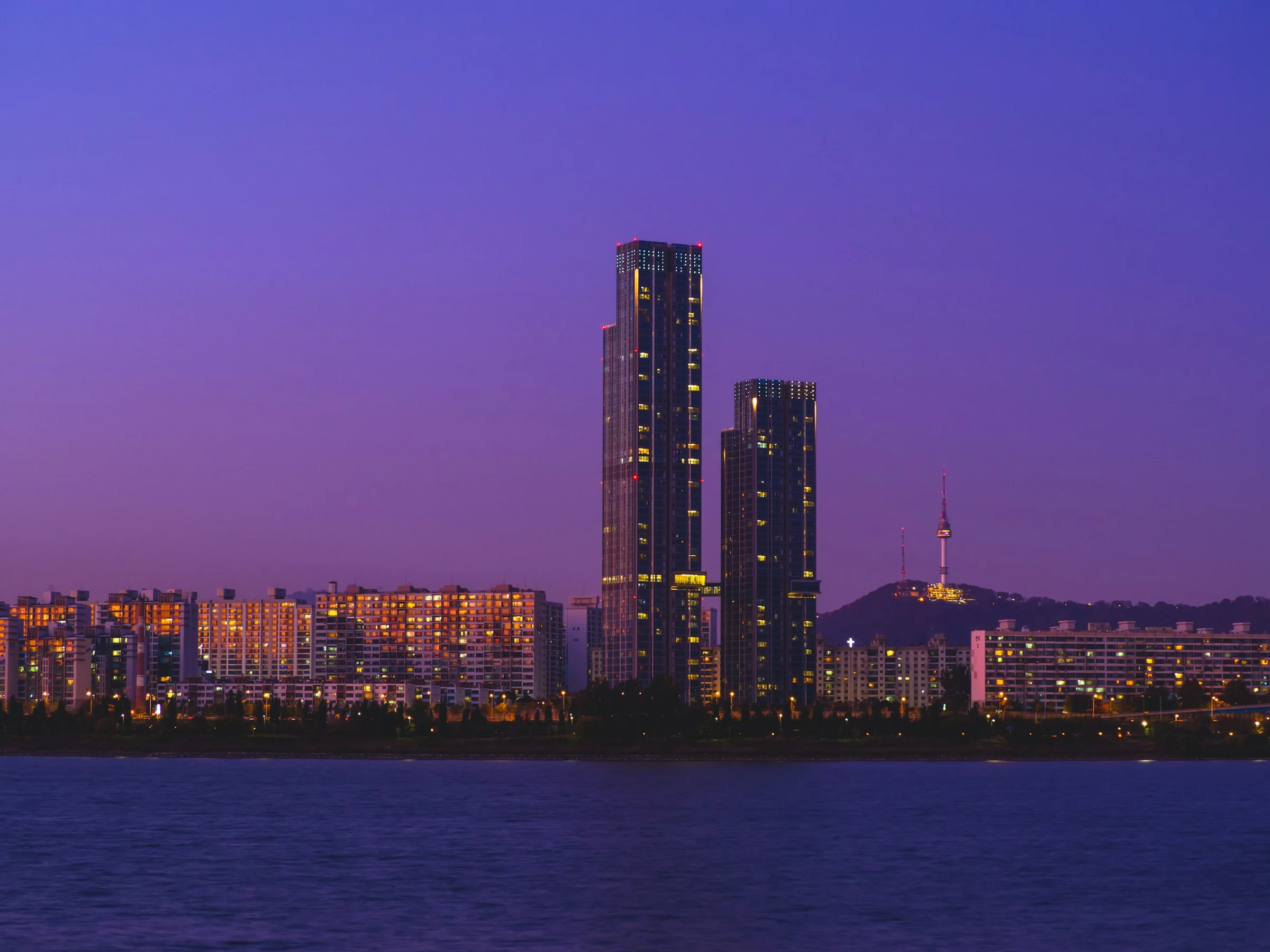 Seoul skyline and N Seoul Tower above the Han River beneath a violet-blue evening sky.