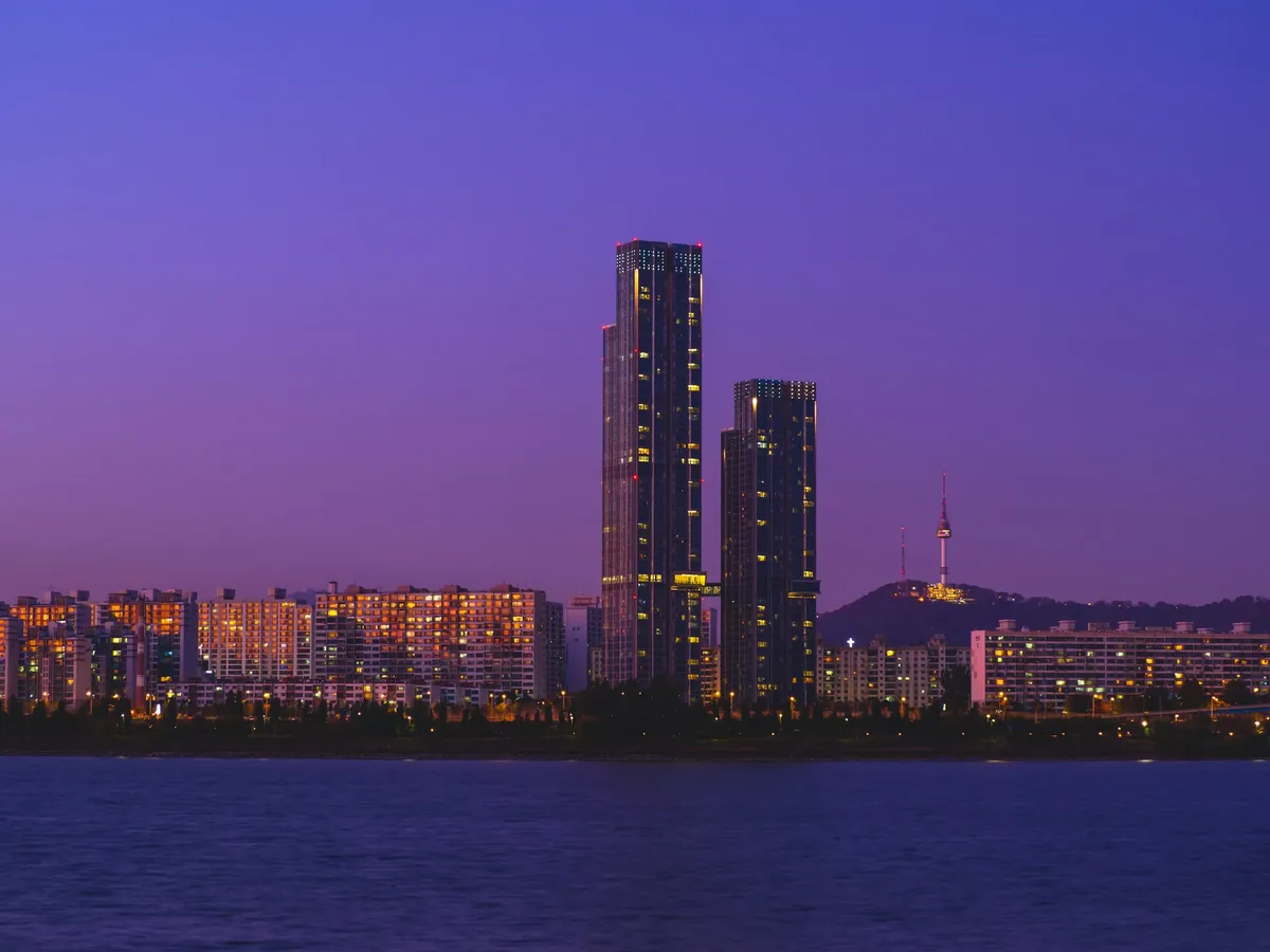 Seoul skyline and N Seoul Tower above the Han River beneath a violet-blue evening sky.